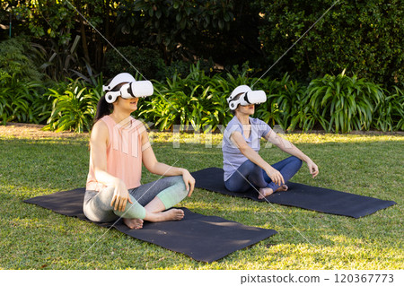 Practicing yoga outdoors, asian grandmother and granddaughter using vr headsets on mats in garden 120367773