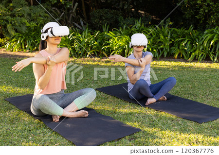 Using VR headsets, asian grandmother and granddaughter stretching on yoga mats in outdoor park 120367776