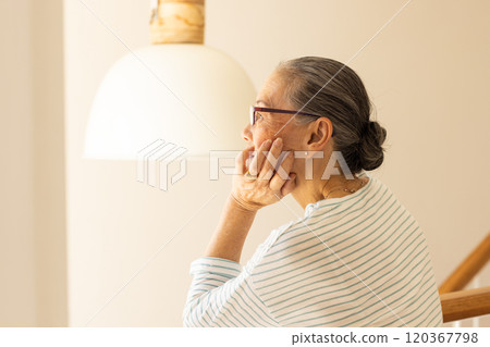 Contemplating, elderly Asian woman with glasses sitting under lamp, looking thoughtful 120367798