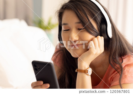 Listening to music with headphones, Asian woman smiling and looking at smartphone 120367801