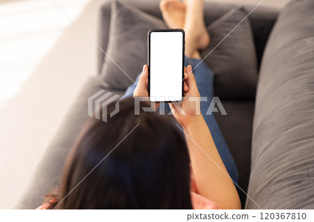 Holding smartphone, Asian woman relaxing on couch and browsing blank screen 120367810