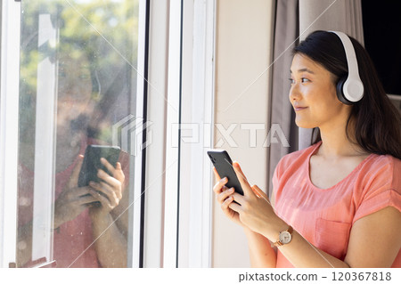 Listening to music on headphones, Asian woman holding smartphone and looking outside, copy space Listening to music on headphones, Asian woman holding smartphone and looking outside, copy space 120367818
