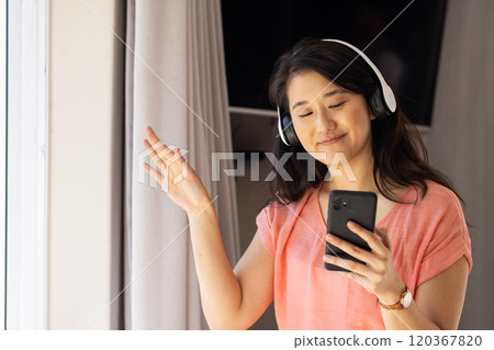 Listening to music on headphones, Asian woman smiling and holding smartphone Listening to music on headphones, Asian woman smiling and holding smartphone 120367820