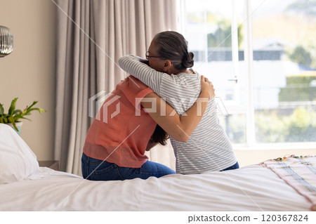 Hugging each other, asian grandmother and granddaughter sitting on bed in cozy bedroom 120367824
