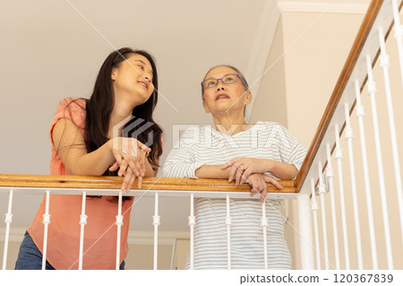 Smiling Asian grandmother and granddaughter leaning on railing, enjoying conversation 120367839
