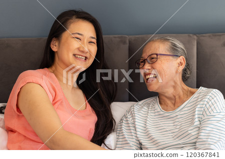 Smiling and laughing, asian grandmother and granddaughter enjoying quality time together on bed 120367841