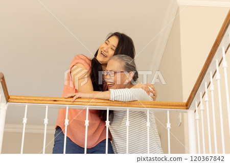 Laughing together, asian grandmother and granddaughter hugging on balcony railing 120367842