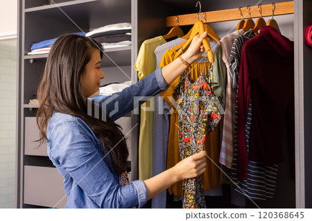 Choosing outfit, asian woman holding dress and looking at clothes in wardrobe 120368645