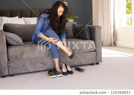 Trying on shoes, asian woman sitting on sofa and adjusting footwear in living room Trying on shoes, asian woman sitting on sofa and adjusting footwear in living room 120368651
