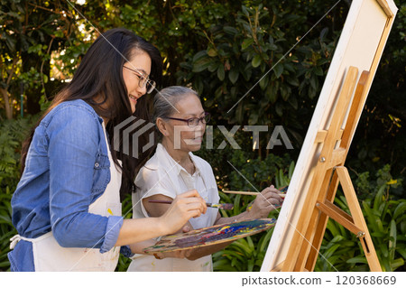 Painting on canvas, Asian granddaughter and grandmother enjoying outdoor art activity together 120368669