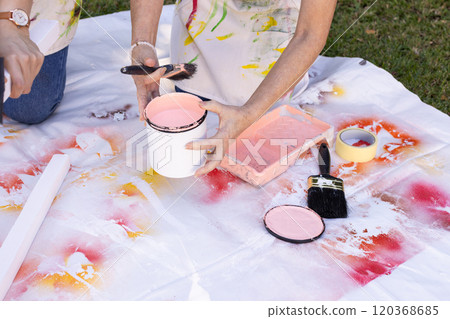 Holding paintbrush and paint can, person painting on canvas, creating artwork outdoors 120368685