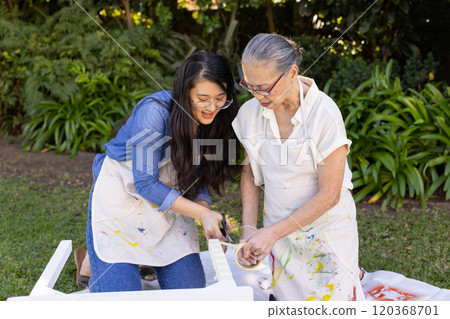 Painting furniture together, asian granddaughter and grandmother enjoying outdoor diy project in gar 120368701