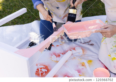 Painting furniture outdoors, two people using brushes and pink paint 120368702