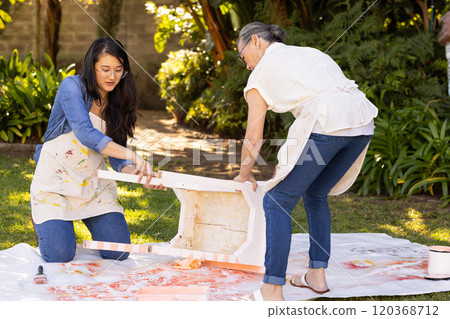 Painting furniture outdoors, asian grandmother and gradndaughter collaborating on DIY project in gar 120368712