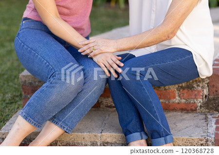 Holding hands, asian grandmother and gradndaughter sitting on steps, showing support and connection 120368728
