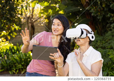 Using VR headset, asian grandmother exploring virtual reality with assistance outdoors 120368735