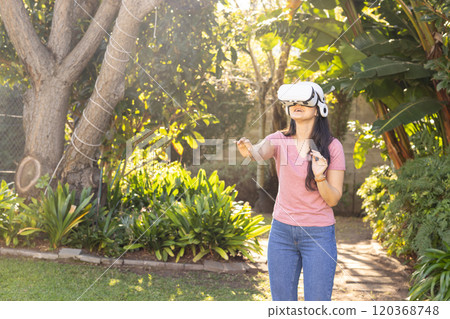 Using VR headset, asian woman exploring virtual reality in lush garden setting 120368748