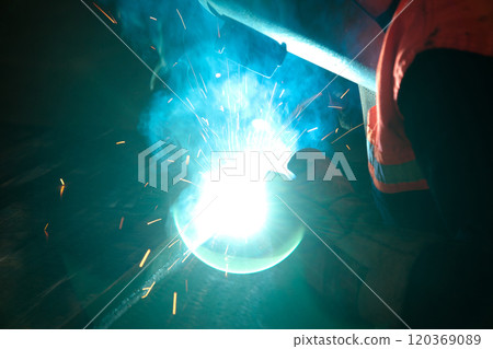Welder uses torch to make sparks during manufacture of metal equipment, industrial professional worker 120369089