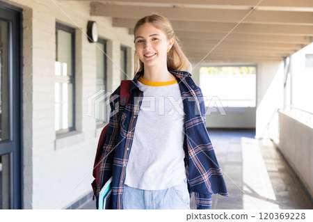 Smiling teenage girl carrying books and backpack, walking in school hallway Smiling teenage girl carrying books and backpack, walking in school hallway 120369228