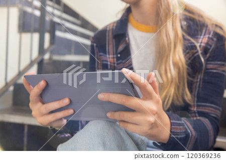 Using tablet, teenage girl sitting on stairs and studying in school environment Using tablet, teenage girl sitting on stairs and studying in school environment 120369236