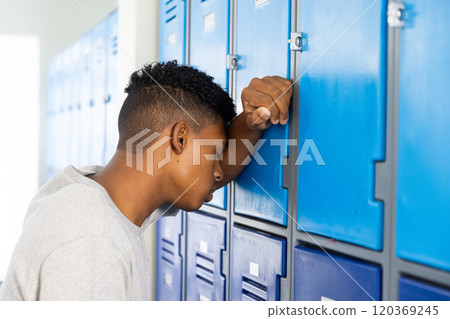 In school, teenage boy leaning against lockers, appearing stressed and overwhelmed In school, teenage boy leaning against lockers, appearing stressed and overwhelmed 120369245