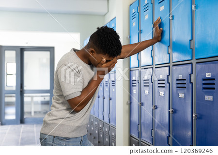 In school, teenage boy leaning against lockers, covering face, feeling stressed In school, teenage boy leaning against lockers, covering face, feeling stressed 120369246