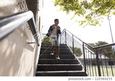 Walking down stairs, teenage boy holding jacket over shoulder at school campus Walking down stairs, teenage boy holding jacket over shoulder at school campus 120369255