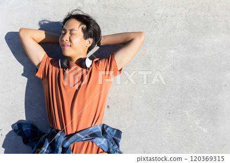 Outdoors, asian teenage boy wearing headphones and orange shirt enjoying sunlight, copy space Outdoors, asian teenage boy wearing headphones and orange shirt enjoying sunlight, copy space 120369315