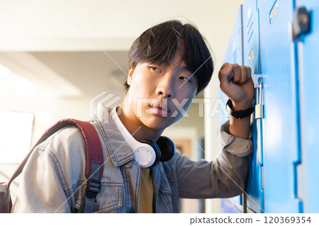 Opening locker, asian teenage boy with headphones looking away in school hallway Opening locker, asian teenage boy with headphones looking away in school hallway 120369354