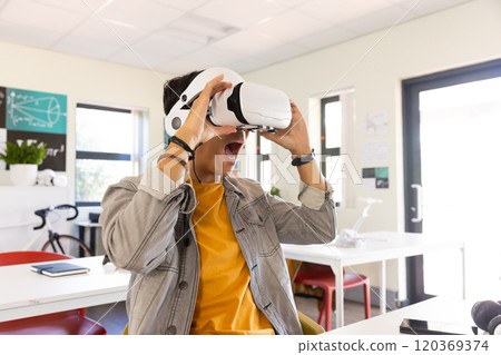 Using VR headset, excited asian teenage boy experiencing virtual reality in school classroom Using VR headset, excited asian teenage boy experiencing virtual reality in school classroom 120369374