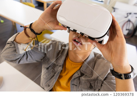 Using VR headset, asian teenage boy exploring virtual reality in school classroom 120369378