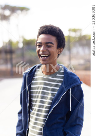 Smiling african american teenage boy in casual clothes enjoying outdoor hangout with friends 120369395
