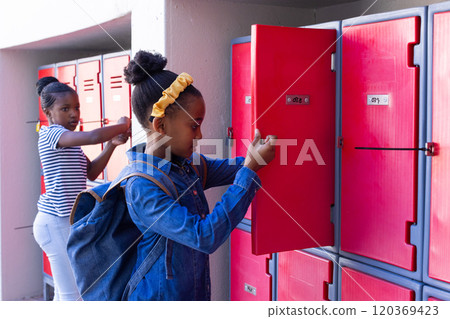 Opening lockers, two school african american girls organizing their belongings in hallway 120369423
