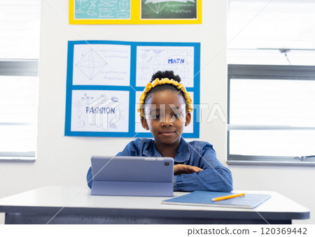 In school, african american girl using tablet at desk, smiling in classroom In school, african american girl using tablet at desk, smiling in classroom 120369442