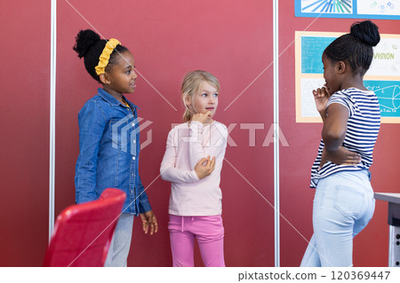 In school, three multiracial girls standing and talking in classroom near posters In school, three multiracial girls standing and talking in classroom near posters 120369447