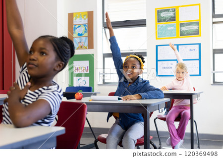 In school, multiracial girls raising hands to answer questions in classroom 120369498