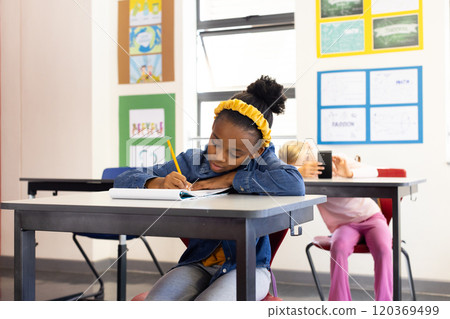 In school, african american girl writing in notebook at desk, focusing on her work In school, african american girl writing in notebook at desk, focusing on her work 120369499