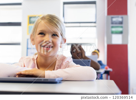 In school, girl smiling and using laptop in classroom, focusing on lesson 120369514