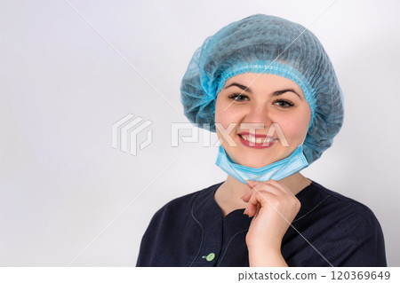 A young nurse in a medical cap and a face mask is smiling 120369649
