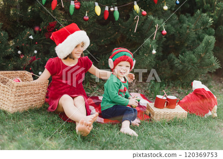 Merry Christmas. Portrait of funny children girls in Santa hat eating gingerbread cookies drinking hot chocolate outside having fun. Happy Holidays. kids enjoying holiday. Christmas in July Merry Christmas. Portrait of funny children girls in Santa hat eating gingerbread cookies drinking hot chocolate outside having fun. Happy Holidays. kids enjoying holiday. Christmas in July 120369753