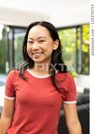 Smiling young asian woman in casual red shirt standing indoors, looking at camera Smiling young asian woman in casual red shirt standing indoors, looking at camera 120370753