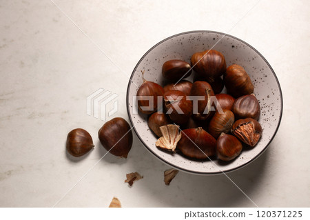 Delicious edible chestnuts in a small bowl on a white table 120371225