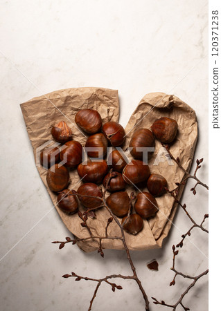 Fresh harvest of edible chestnuts scattered on a on kraft paper with tree branches Fresh harvest of edible chestnuts scattered on a on kraft paper with tree branches 120371238