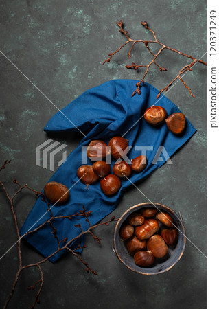 A bowl with edible chestnuts stands on a blue cloth 120371249