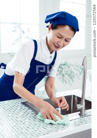 Senior female housekeeper cleaning the kitchen 120372564