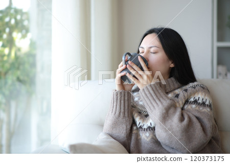 Asian woman in winter drinking coffee or tea at home Asian woman in winter drinking coffee or tea at home 120373175