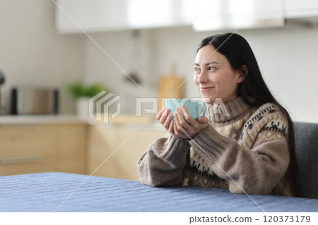 Asian woman relaxing in the kitchen in winter drinking tea Asian woman relaxing in the kitchen in winter drinking tea 120373179