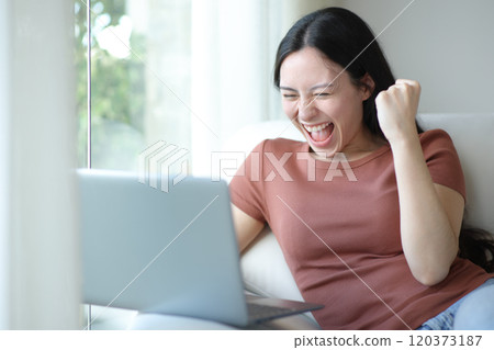 Excited asian woman using laptop at home 120373187