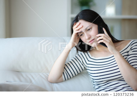 Worried asian woman talking on phone at home 120373236