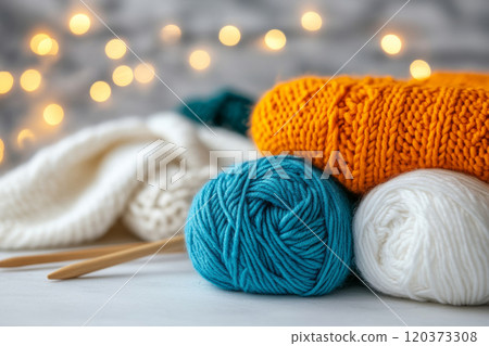 Yarn balls, knitting needles, and a folded knitted scarf with blurred lights 120373308